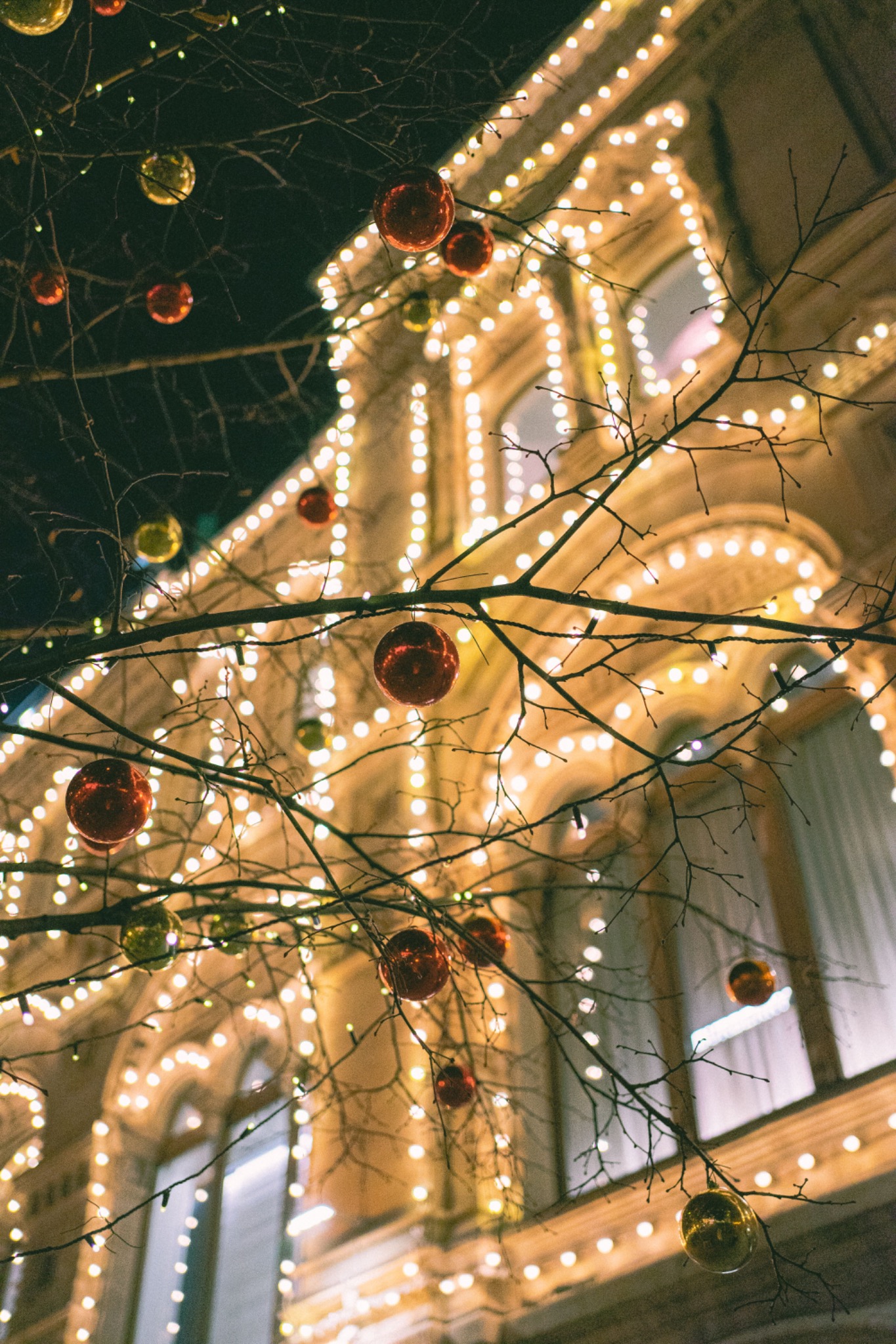 Warm white holiday lighting outlining ornate architecture with Christmas ornaments in the foreground